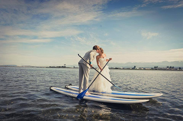 bride and groom kissing while on surfing board