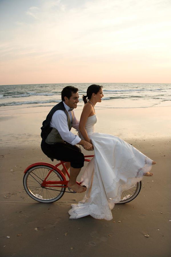 bride and groom riding a red bike at beach