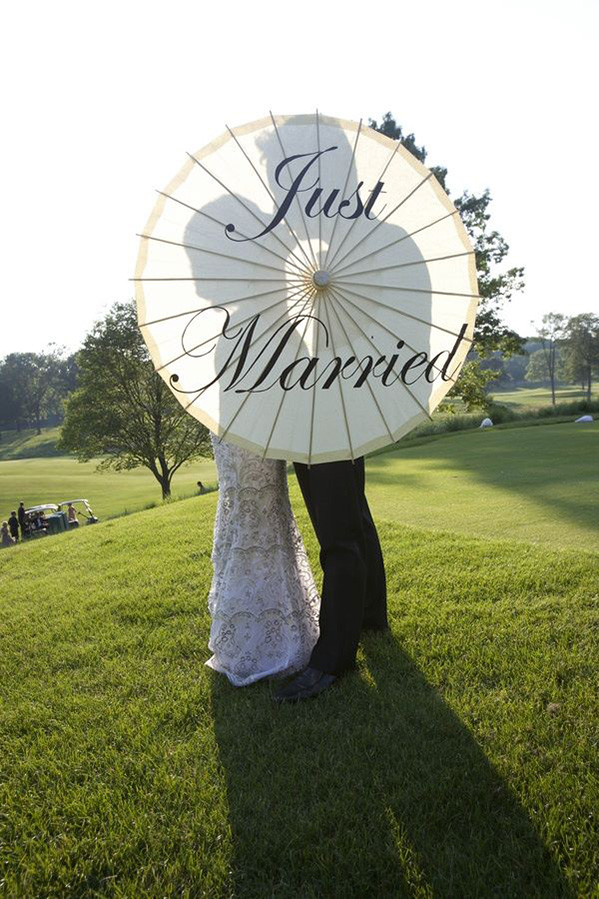 wedding couple is posing behind a just married umbrella