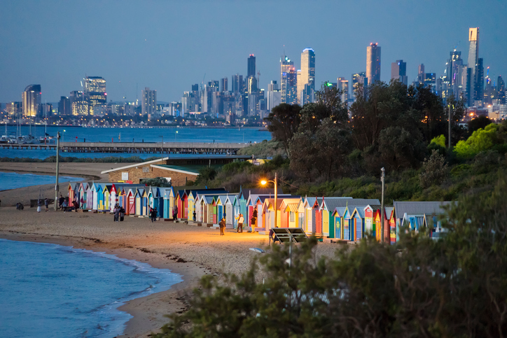Visitors around beach boxes at Brighton Beach at dusk.